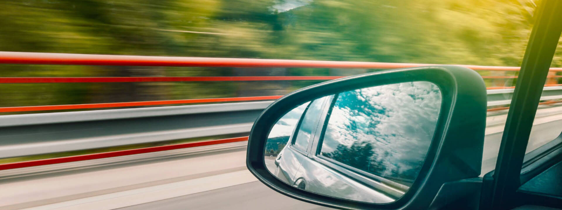 Car left side mirror with sky and trees reflecting in it